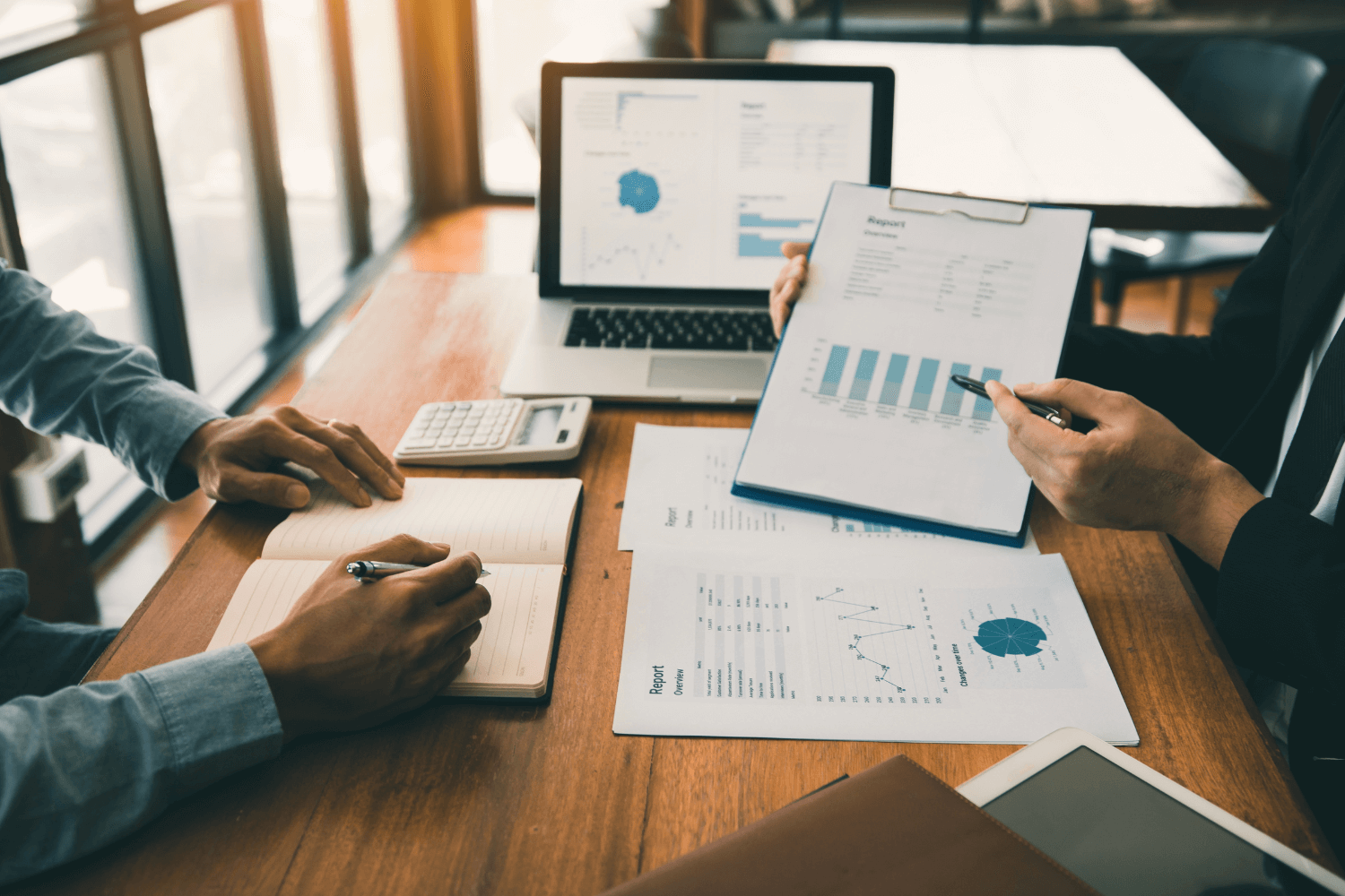 Two business professionals review a marketing audit report from The Brand Coach at a table with papers and a laptop.