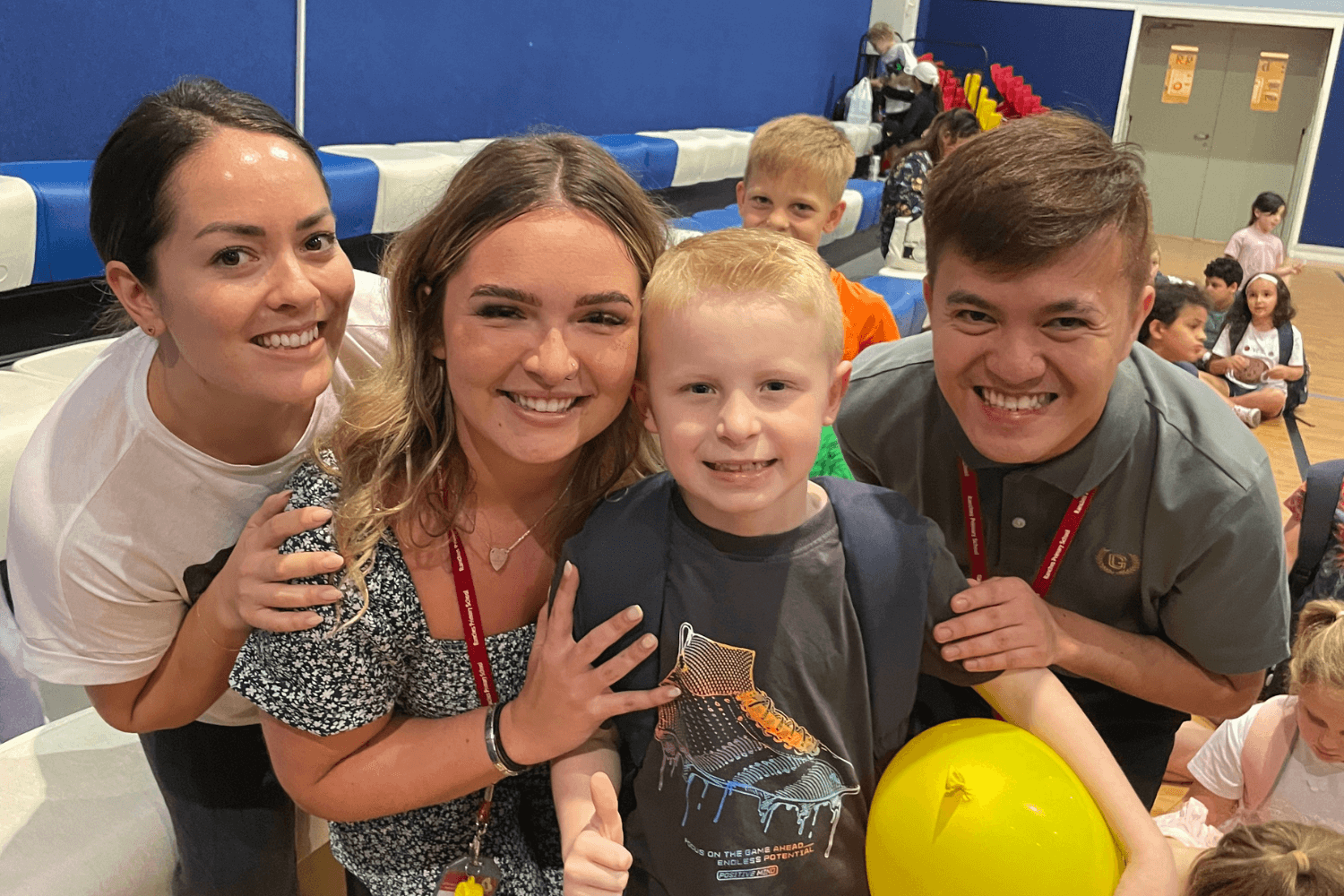 Young boy celebrating his last day of school, smiling with three teachers in a school hall
