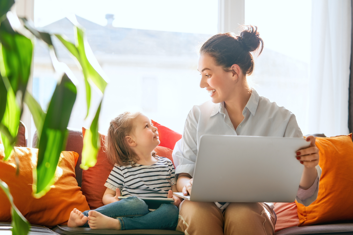Female entrepreneur working on a laptop at home while her child plays beside her